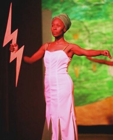Black female artiste on stage with arms outstretched in white dress
