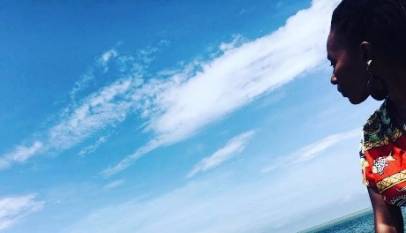 Back woman sitting on seawall looking seawards with blue sky above