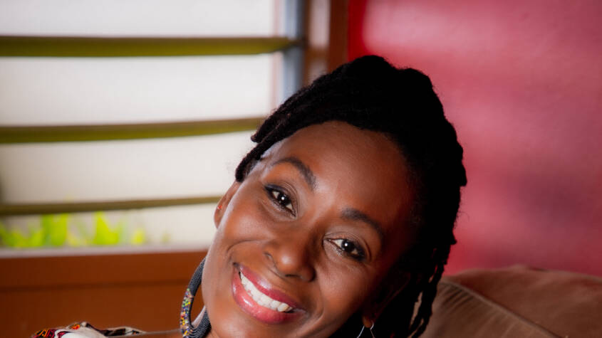 Black woman in African top and blue jeans sitting and smiling