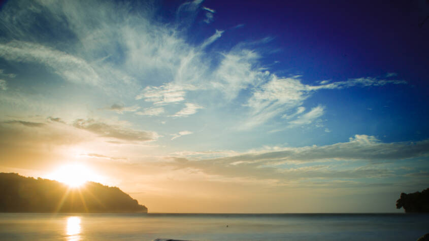 Fishing boat on beach with sun about to rise above mountain in distance